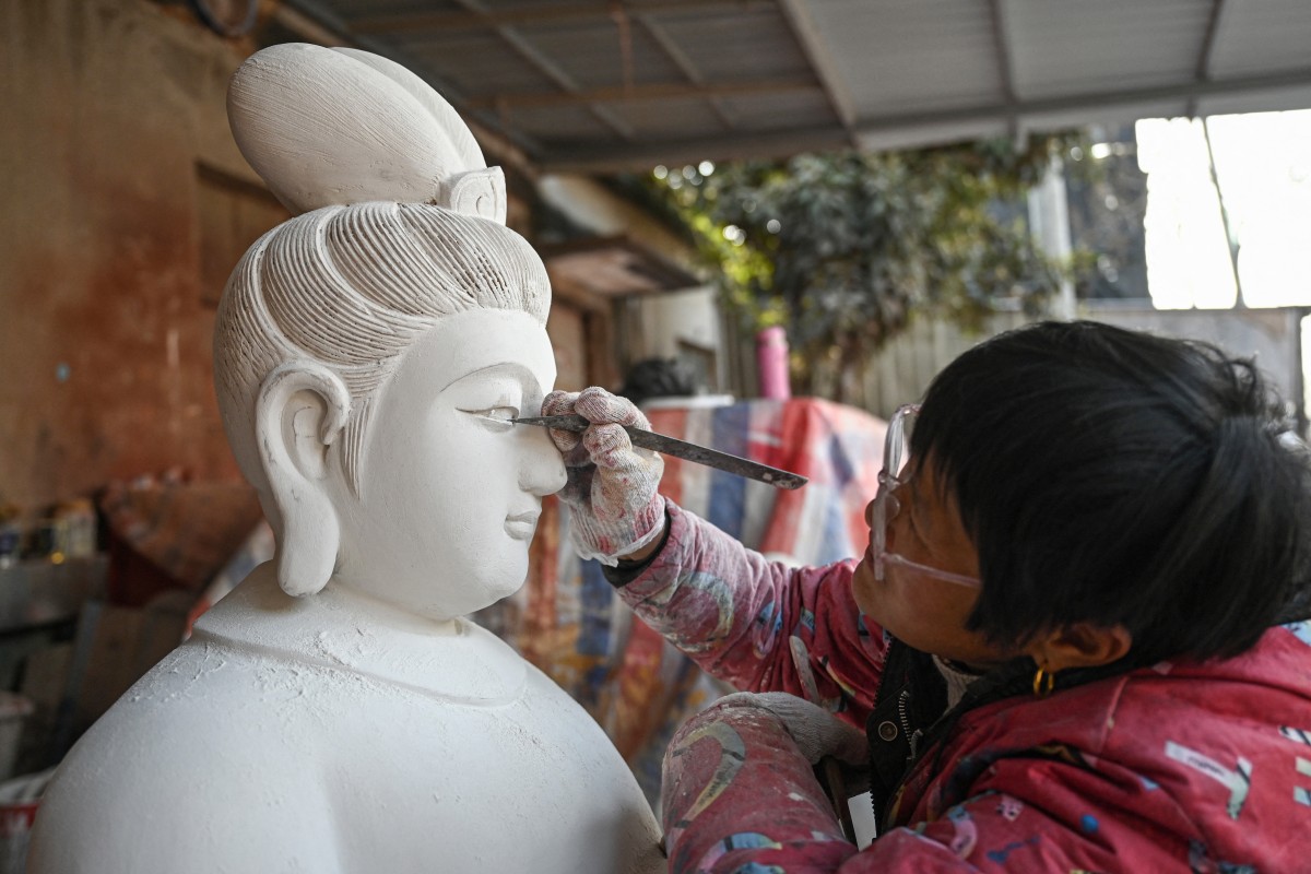 In this picture taken on January 16, 2026, an artisan carves a wooden Bodhisattva sculpture at a workshop in Chongshan village, Suzhou, in eastern China's Jiangsu province. (Photo by JADE GAO / AFP)