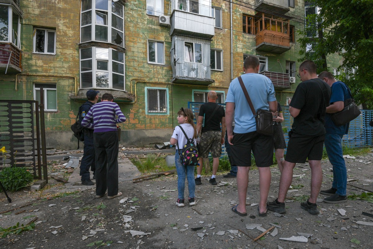 Local residents stand next to debris and a damaged residential building following an air attack in Dnipro on May 21, 2026, amid the Russian invasion of Ukraine. (Photo by Mykola SYNELNYKOV / AFP)