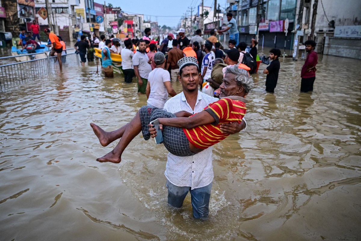 A youth carries an elderly man as they wade through a flooded street after heavy rainfall in Wellampitiya on the outskirts of Colombo on November 30, 2025. (AFP)