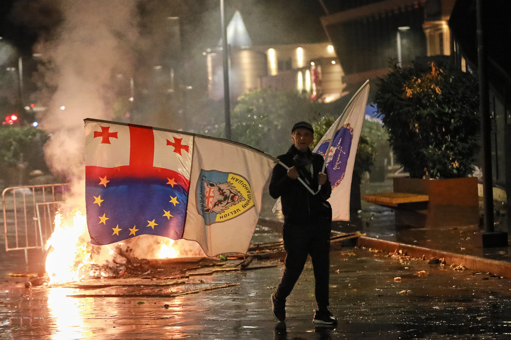 A demonstrator with a Georgian national, EU and other flags walks in front of police line during an opposition rally in the city center of Tbilisi, Georgia, on Saturday, Oct. 4, 2025, boycotting the municipal elections and calling for the release of polit