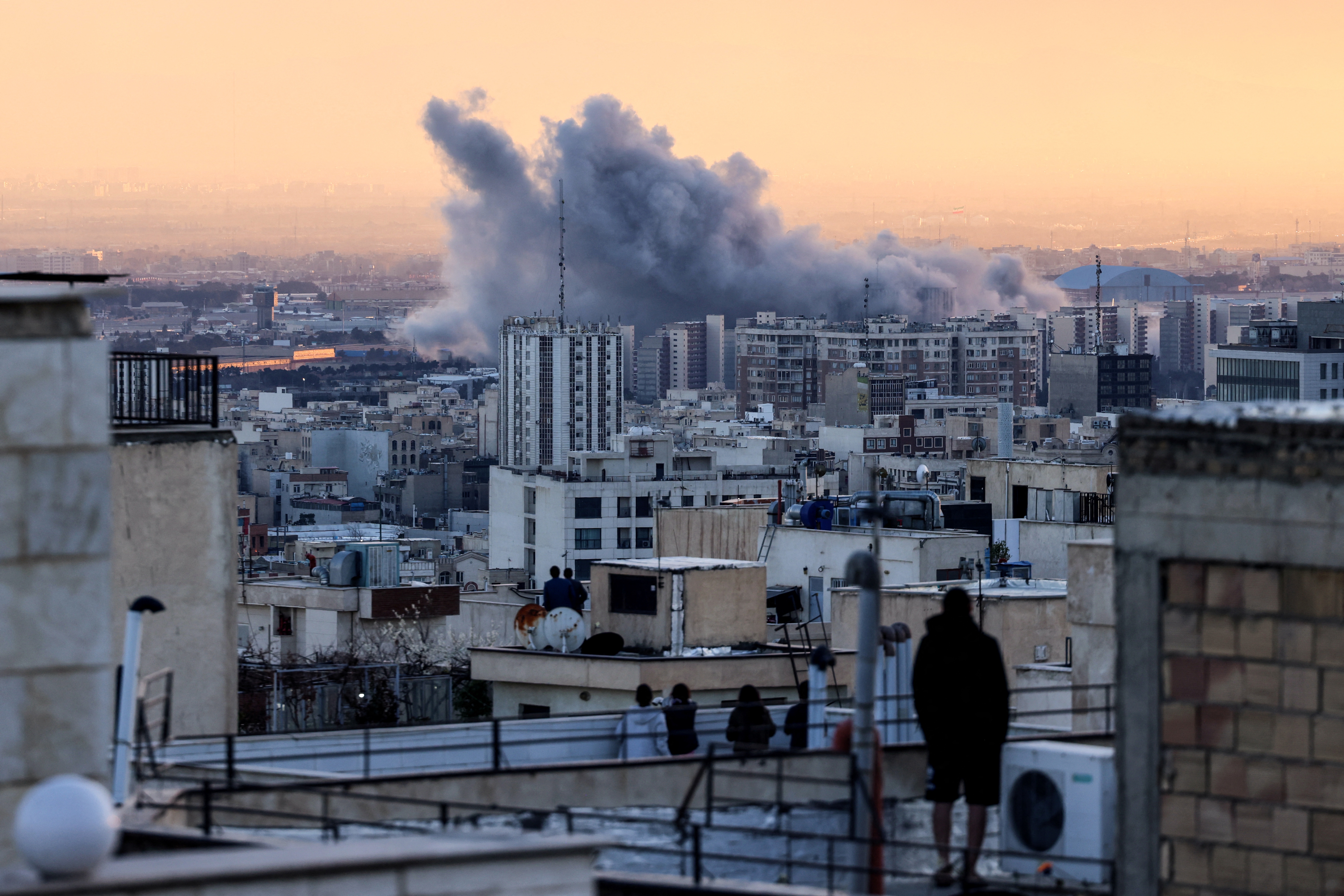 A person stands on the roof of a building looking at a plume of smoke rises after a strike on the Iranian capital Tehran. (AFP)
