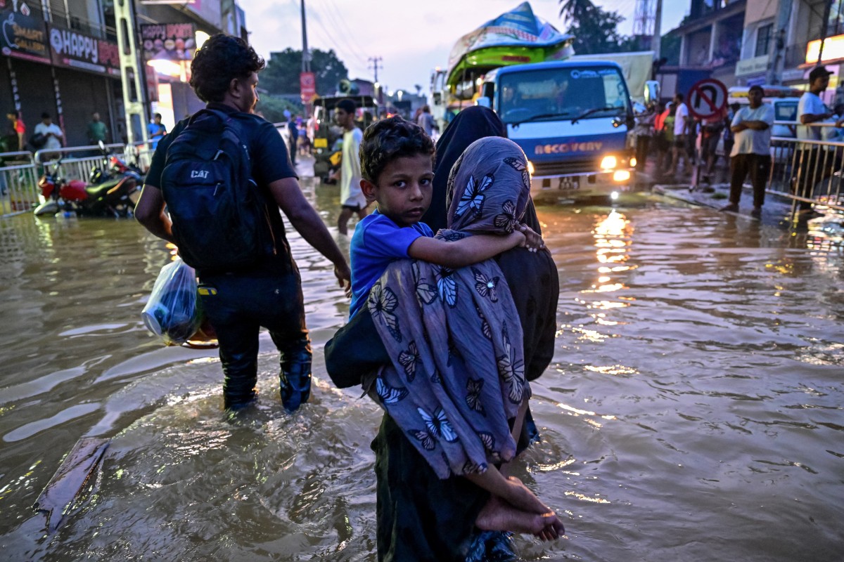 A woman carrying a child wades through a flooded street after heavy rainfall in Wellampitiya on the outskirts of Colombo on November 30, 2025, after a powerful cyclone. (AFP)