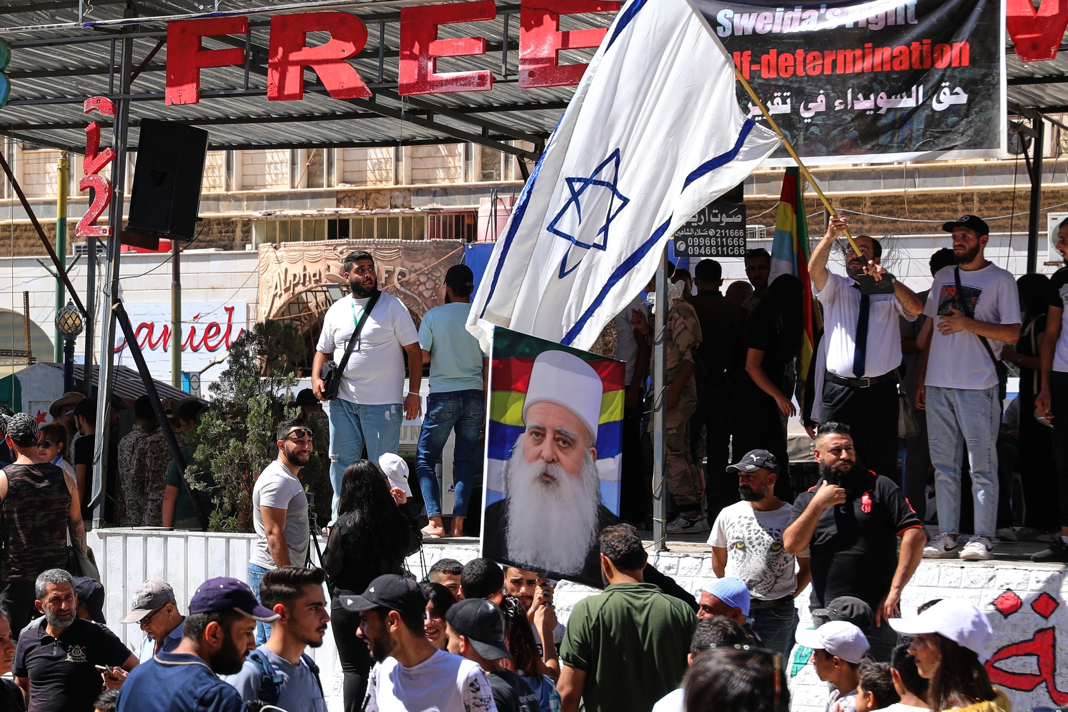 A man waves an Israeli flag over a picture of Sheikh Mowafak Tarif, the spiritual leader of the Druze in Israel, during a weekly rally in Sweida, southern Syria, on Sept. 20, 2025. (AP Photo/Fahd Kiwan)