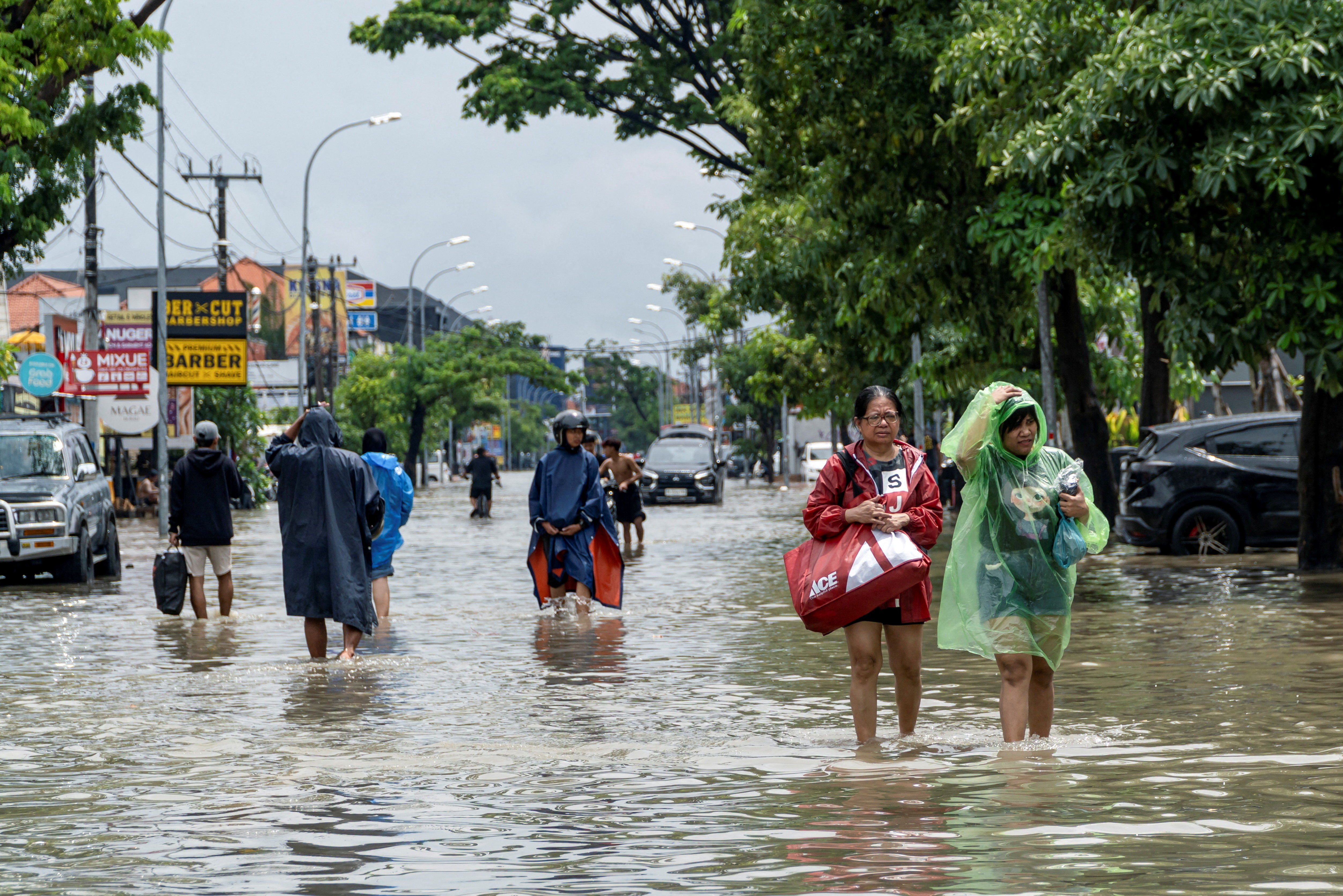 People carrying their belongings wade through a flooded street